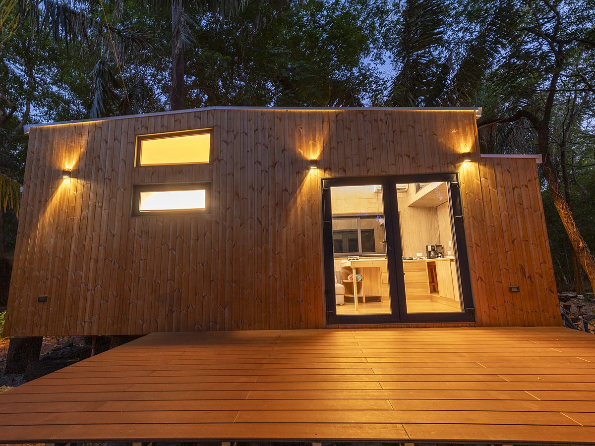 Aurora — wooden tiny home glowing at dusk under the jungle canopy
